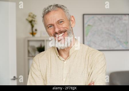 Lächelnder, reifer bärtiger Mann, der zu Hause auf die Kamera schaut, ein Kopfbildnis. Stockfoto