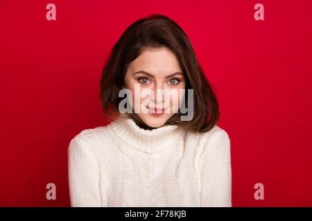 Portrait von attraktiven Brünette fröhlich schüchtern niedliches Mädchen tragen gemütlich Wolle weiße Kleidung isoliert über leuchtend roten Hintergrund Stockfoto