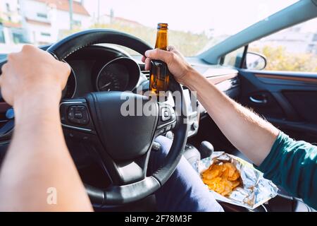 Ein junger betrunkener Mann fährt mit einer Flasche Bier ein Auto. Fahren unter Alkoholeinfluss. Betrunkene Fahrweise Stockfoto