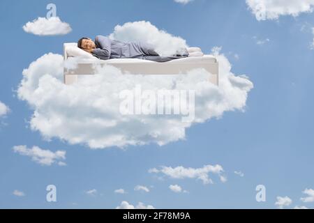 Mann schläft friedlich in den Wolken, die auf seinem schweben Bett Stockfoto