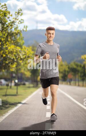 Ganzkörperportrait eines Mannes, der auf einem Asphalt joggt Fahrspur Stockfoto