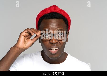 Unsicher, zweifelhafter afroamerikanischer Mann in rotem Hut, der eine Brille hält, Gleichaltrige, misstrauisch, der die Kamera anschaut Stockfoto