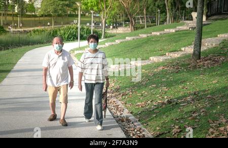 Ein erfahrenes asiatisches Paar mit Gesichtsmaske bei einem Spaziergang in einem grünen Park. Gesunder Lebensstil während des Pandemiekonzepts. Stockfoto