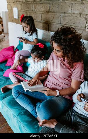 Junge lateinerin und ihre kleinen Kinder lesen bei Zuhause in Mexiko-Stadt Stockfoto