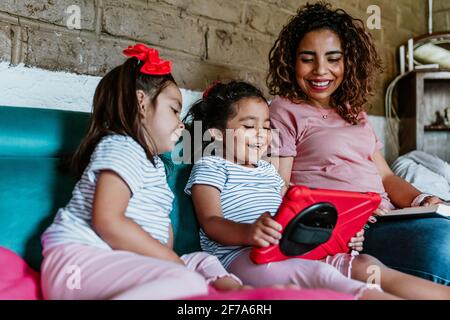 Junge lateinerin und ihre kleinen Kinder lesen bei Zuhause in Mexiko-Stadt Stockfoto