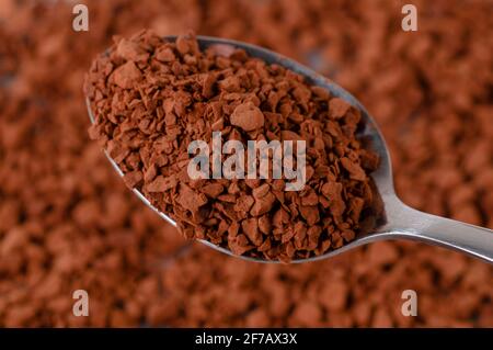 Instant-Kaffee-Granulat liegt auf der Oberfläche. Der Löffel enthält trockenes Granulat von Instant-Kaffee. Stockfoto