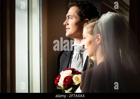 Brautpaar steht am Fenster auf ihre Hochzeit und suchen außerhalb Stockfoto