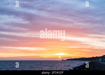 Wolkiger, dramatischer Morgenhimmel mit dem Sonnenaufgang über dem Meer und der Kent-Küste bei Reculver mit den Wahrzeichen-Zwillingstürmen der ruinierten Kirche aus dem 12. Jahrhundert auf der kleinen Landzunge, einem Teil der Sächsischen Küste. Wolkenschichten über dem Meer, die verschiedene Farbgrade reflektieren. Stockfoto