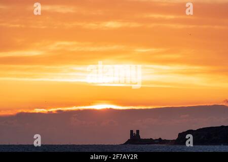 Wolkiger, dramatischer Morgenhimmel mit dem Sonnenaufgang über dem Meer und der Kent-Küste bei Reculver mit den Wahrzeichen-Zwillingstürmen der ruinierten Kirche aus dem 12. Jahrhundert auf der kleinen Landzunge, einem Teil der Sächsischen Küste. Wolkenschichten über dem Meer, die verschiedene Farbgrade reflektieren. Stockfoto