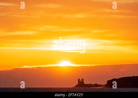 Wolkiger, dramatischer Morgenhimmel mit dem Sonnenaufgang über dem Meer und der Kent-Küste bei Reculver mit den Wahrzeichen-Zwillingstürmen der ruinierten Kirche aus dem 12. Jahrhundert auf der kleinen Landzunge, einem Teil der Sächsischen Küste. Wolkenschichten über dem Meer, die verschiedene Farbgrade reflektieren. Stockfoto