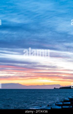 Wolkiger, dramatischer Morgenhimmel über dem Meer und der Küste von Kent in Reculver mit den Wahrzeichen-Zwillingstürmen der ruinierten Kirche aus dem 12. Jahrhundert auf der kleinen Landzunge, die an der Sächsischen Küste liegt. Wolkenschichten über dem Meer, die verschiedene Farbgrade reflektieren. Stockfoto