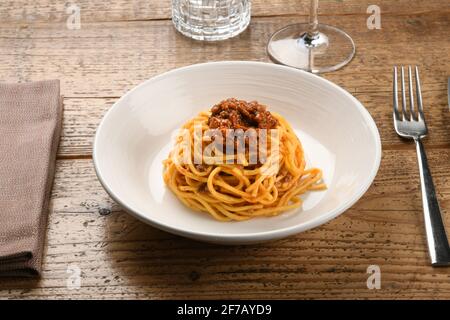 Servieren von Wildschweinragout auf Tagliolini oder Spaghetti Italienisch Pasta auf einem Holztisch mit Gläsern und Utensilien Ein Konzept der regionalen Spezialität Stockfoto