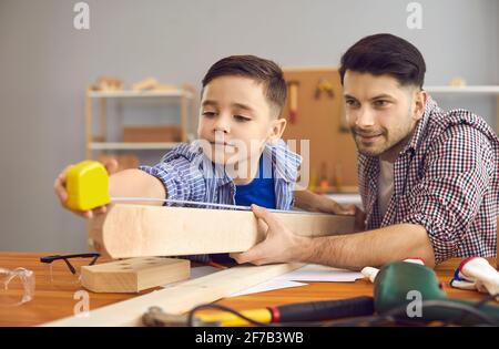 Glücklicher kaukasischer Vater und Sohn, der Holzplanke mit Klebeband misst In der Werkstatt zu Hause Stockfoto