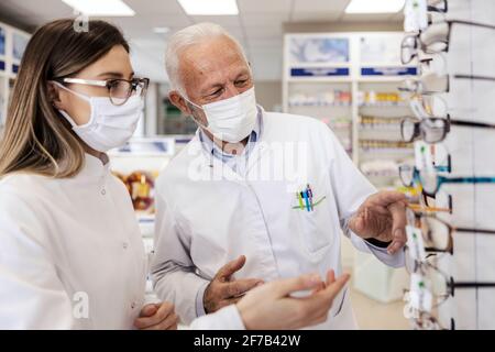 Gespräch von zwei Apothekern über Dioptrien für Gläser. Eine Frau mit Brille und ein älterer Mann stapeln Gläser in einer Apotheke. Sie tragen weiße Uniformen a Stockfoto