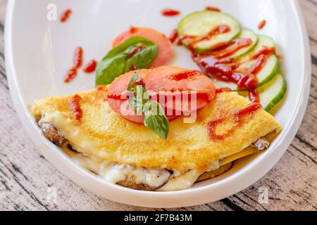 Eine leckere, herzhafte Kreppe mit Auberginen, Zucchini und Tomaten auf einem weißen Teller, mit Basilikumblättern verziert Stockfoto