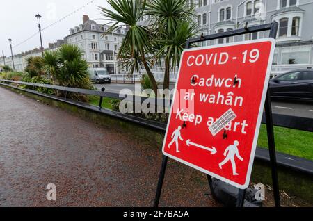 Llandudno, Großbritannien: 18. März 2021: Ein zweisprachiges Schild an der Promenade erinnert Fußgänger daran, sich während der Coronavirus-Sperre auseinanderzuhalten Stockfoto