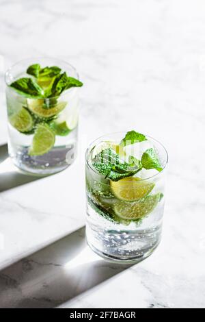 Mojito-Cocktail mit Minze und Limette in Gläsern, Hintergrund aus weißem Marmor. Erfrischendes Getränk mit Limette und Minze in Gläsern. Stockfoto