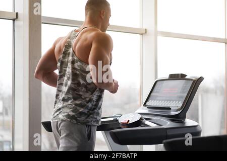 Muskulös athletisch Bodybuilder Fitness-Modell Laufband Fitness-Studio in der Nähe von großen Fenster Jogging-Stationärmaschine tun Cardio-Training Gewichtsverlust gesunde Lebensweise Konzept. Rückansicht hinten Stockfoto