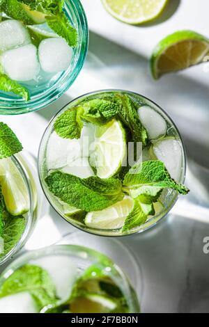 Mojito Cocktail mit Minze und Limette in verschiedenen Gläsern, weißer Marmorhintergrund. Erfrischendes Getränk mit Limette und Minze in Gläsern. Stockfoto