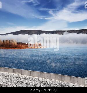 Winter frostiger Nebel auf einem ungefrorenen Fluss. Bäume und Gras am Ufer. Landschaft Natur. Stockfoto