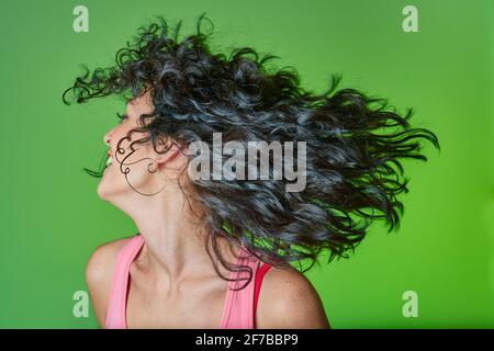 Lächelnde junge Frau mit lockigen schwarzen Haaren nach lockigen Mädchen Methode für die Pflege für ihre Locken und Haare. Haarpflegekonzept. Grüner Hintergrund. Stockfoto