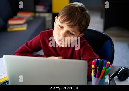 Vorderansicht des gelangweilten Jungen während des Studiums zu Hause Stockfoto
