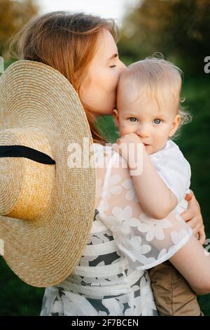 Eine liebevolle junge Mutter hält den Jungen in ihren Armen und umarmt ihn, das Kind blickt in die Kamera. Stockfoto