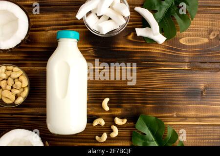 Kokosmilch in der Glasflasche und Cashewnüsse auf dem braunen Holzhintergrund.Draufsicht.Platz kopieren. Stockfoto