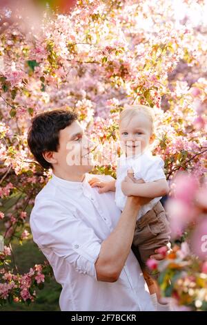 Porträt eines glücklichen Vaters und Sohnes vor dem Hintergrund eines blühenden Gartens im Park. Stockfoto