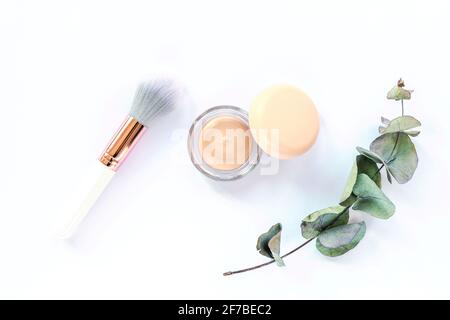 Concealer, Make-up Pinsel und grüner Eukalyptuszweig auf weißem Hintergrund. Draufsicht, flach liegend. Konzept der Naturkosmetik Stockfoto