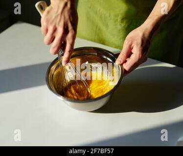 Hausgemachte Kuchen backen, Oster-Kuchen vorbereiten oder Cookie-Konzept. Koch in grüner Schürze, der Zucker und Eier in einer Metallschüssel mit Drahtbesen mischt. Hochwertige Fotos Stockfoto