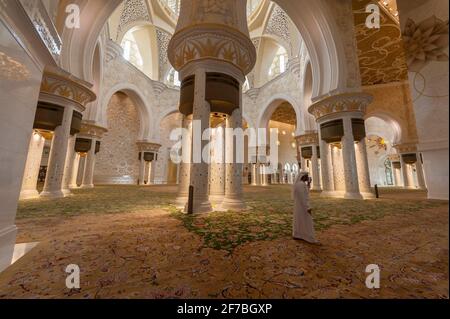 Mann mit Handy läuft in der Gebetshalle der Scheich-Zayed-Moschee in Abu Dhabi, Vereinigte Arabische Emirate. Stockfoto