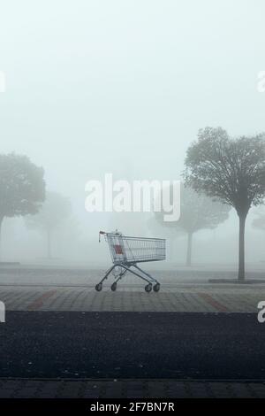 Verlassene Warenkorb auf Parkplatz in dichtem Nebel. Themen Einkaufen, Finanzkrise und Armut. Stockfoto
