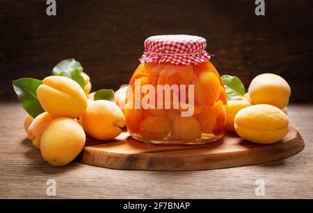 Glas mit Aprikosen in Dosen und frischen Früchten auf einem Holztisch Stockfoto
