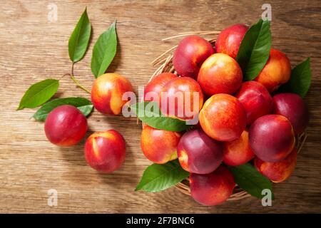 Frische reife Nektarinen mit Blättern auf einem Holztisch, Draufsicht Stockfoto