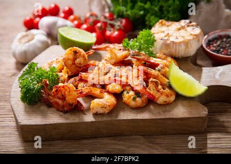 Gegrillte Garnelen mit Limette und Petersilie auf einem Holzbrett Stockfoto