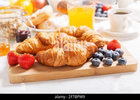 Frühstück mit Croissants, Kaffee, Saft, Marmelade, Müsli und frischem Obst auf einem Holztisch Stockfoto