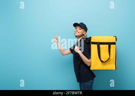 Fröhlicher Kurier, der den Daumen nach oben zeigt, während er den Thermorucksack trägt Blau Stockfoto