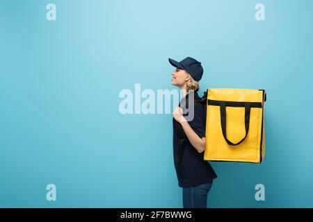 Seitenansicht des glücklichen Kuriers, der Thermorucksack auf Blau trägt Stockfoto