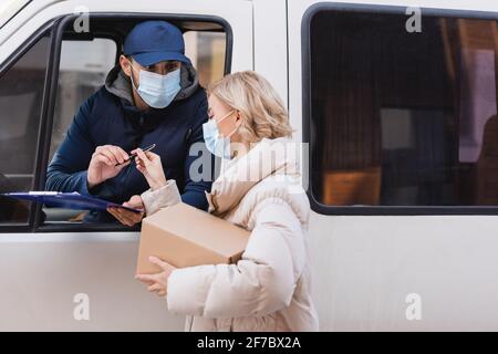 muslimischer Kurier in medizinischer Maske, der der Frau Stift in der Hand gab Paket Stockfoto