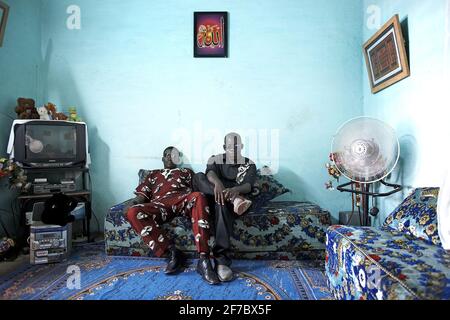 Zwei Mann sitzen auf dem Sofa neben dem Fernseher im Wohnzimmer, Bamako Mali, Westafrika. Stockfoto