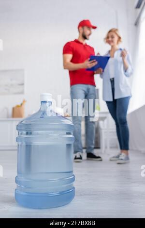 Selektiver Fokus der großen Flasche reines Wasser in der Nähe von arabian Kurier und Frau auf verschwommenem Hintergrund Stockfoto