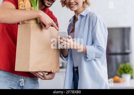 Beschnittene Ansicht des Zustellers, der auf das Smartphone in den Händen zeigt Des Kunden Stockfoto