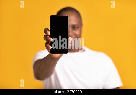 Fröhlicher afroamerikanischer Mann mittleren Alters in weißen T-Shirt-Shows Smartphone mit leerem Bildschirm Stockfoto