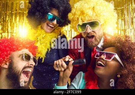 Gruppe von glücklichen Freunden in lustigen Kostümen singen und haben Spaß bei Karaoke-Party Stockfoto
