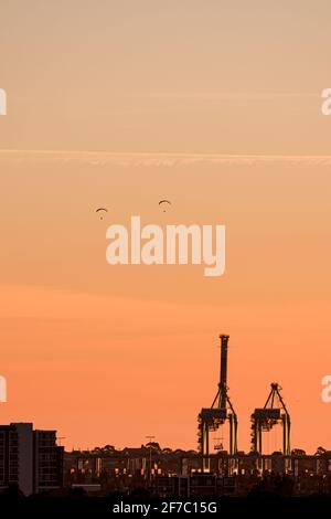 Ein Paar Gleitschirmflieger segelt am Strand von Port Melbourne vorbei, mit den Hafenhöfen von Port Melbourne im Hintergrund. Stockfoto