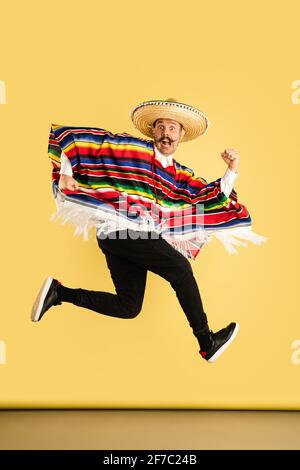 Glücklicher Mann in Sombrero und hellem Poncho über Gelb isoliert Hintergrund Stockfoto