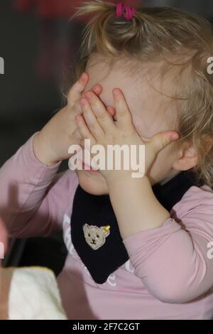 kleines Mädchen spielt verstecken, indem es sich die Hände vor die Augen hält - kleines Mädchen spielt sich verstecken, indem es ihre Hände vor ihr hält Stockfoto