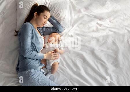 Co-Sleeping mit Baby. Junge Frau, die mit ihrem neugeborenen Kind im Bett schlappte Stockfoto