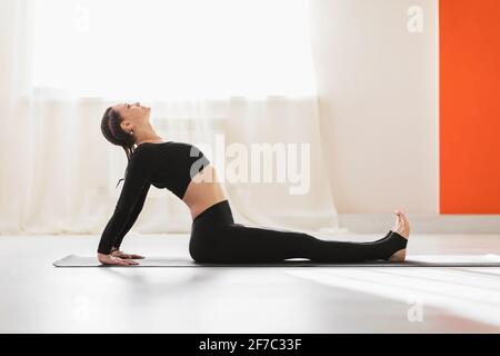 Eine attraktive Frau mittleren Alters in schwarzer Sportkleidung, die Yoga praktiziert, führt ein vorbereitendes Warm-up für die Purvottanasana oder umgekehrte Plank-Übung durch. Stockfoto